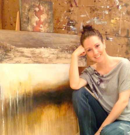 A photo of Donna Giraud in her studio kneeling next to one of her paintings.